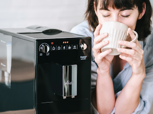 Aromatischer Kaffeegenuss (03)1.png – Melitta® Lifestyle – Woman sitting at table smiling with coffee mug in hand